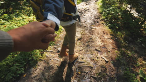 a couple of tourists hold hands and walk on a slippery stony path in the forest only the legs are vi