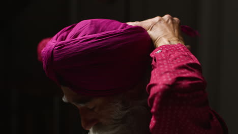 close up low key studio lighting shot of senior sikh man with beard using salai needle when putting on turban against dark background 2