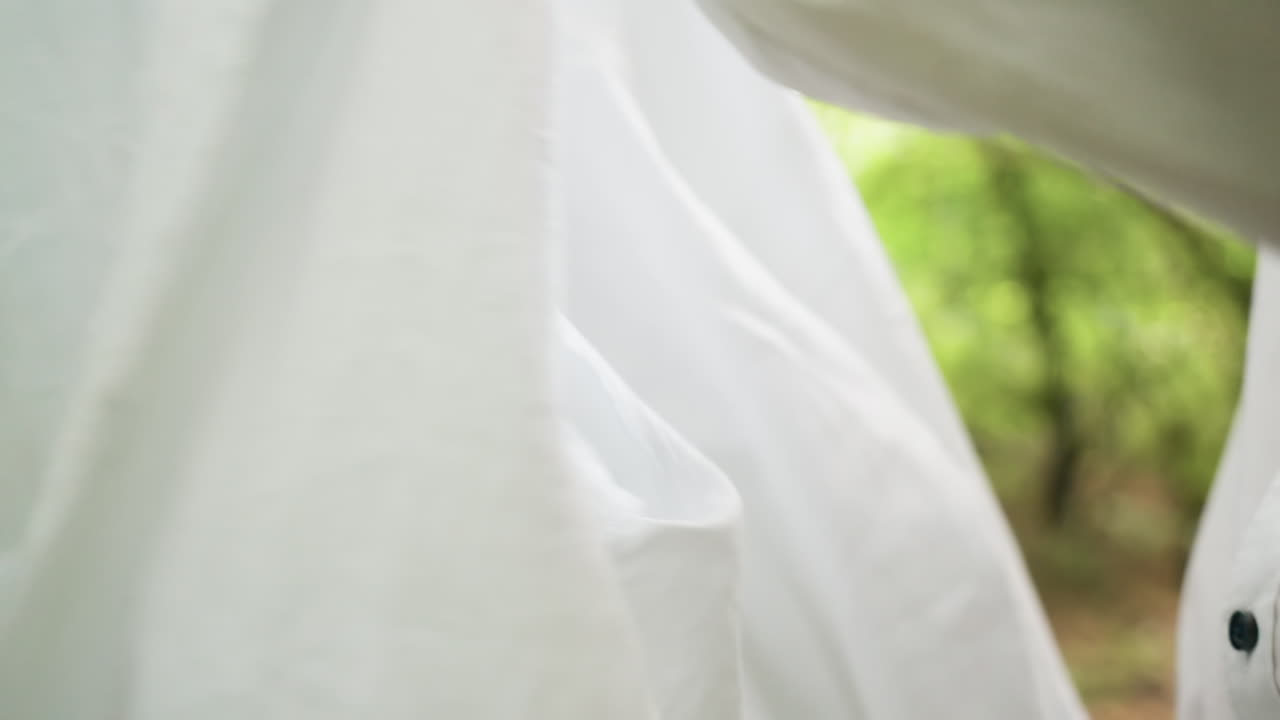 Close up view of man in white shirt pulling off coat outdoors in forest, with blurred natural background, emphasizing movement, detail, and lifestyle moment of preparation in woodland environment