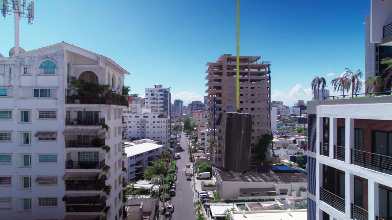Ripresa aerea con drone dall'alto in ascesa su un canyon urbano di strada, che mostra moderni edifici residenziali e un grattacielo in costruzione con una gru che solleva materiali alla luce del giorno.
