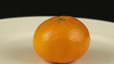 Close-up-orange-revolves-on-white-plate-against-black-background