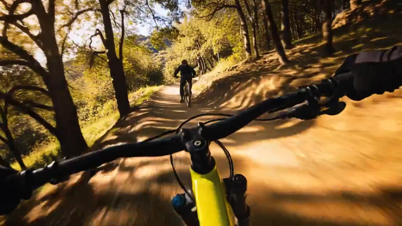 Ciclista em perseguição ajusta o guidão e a velocidade na trilha enquanto o líder pedala, diminuindo a distância com a bicicleta de quadro amarelo.