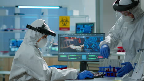 médico biólogo en traje de ppe comprobando muestra de líquido escribiendo en pc