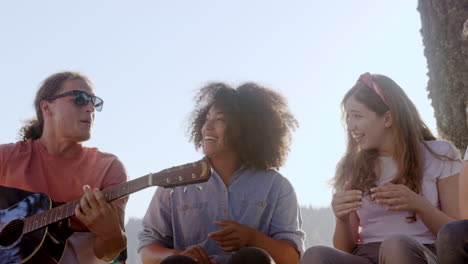 amigos cantan y tocan la guitarra junto al lago
