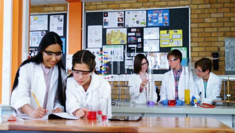 school girls writing in journal book while experimenting in laboratory at school