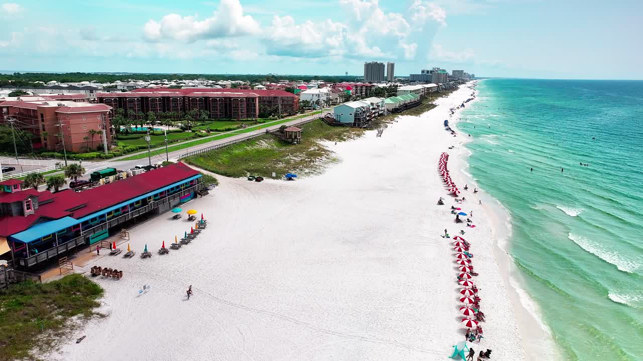 Pompano Joe's restaurant and parking lot aerial drone shot with a view of old 98, white sand, emerald green water and lots of umbrellas and beach chairs in Destin FL