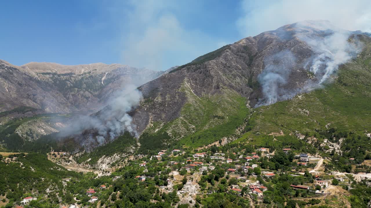 Wildfires burning side of the mountain releasing smoke and ash in the air and getting close to the village nearby