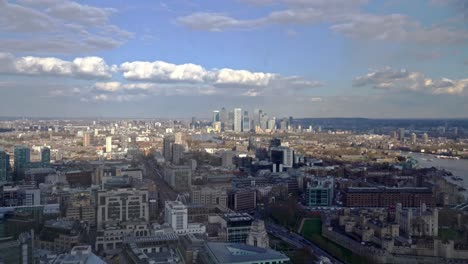 Aerial-panning-shot-showing-London-Canary-Wharf-Cityscape-with-high-rising-buildings-and-River-Thames