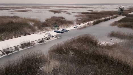 aerial view of a frozen marshland with patches of ice, brown vegetation, and misty surroundings, creating a cold and desolate winter landscape.