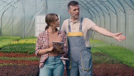 Two-caucasian-botanists-standing-in-the-greenhouse-and-using-digital-tablet