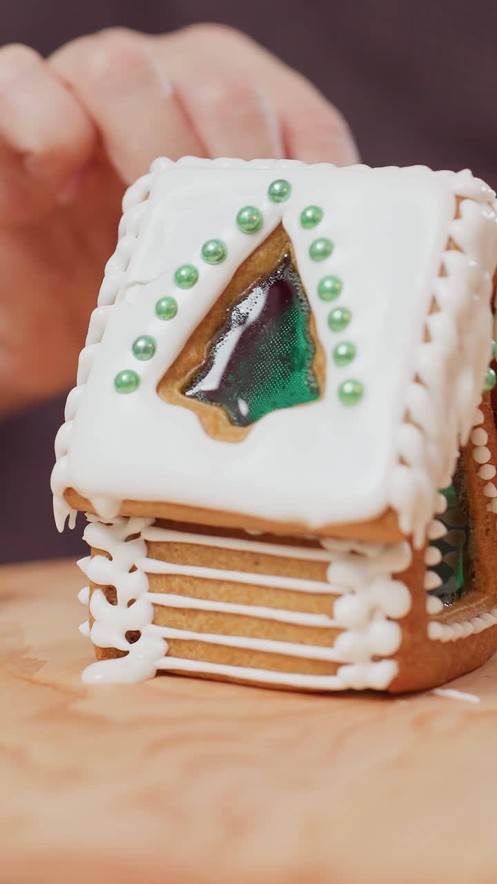 primer plano de una persona que cuida cuidadosamente el pastel de hielo mientras un recipiente de vidrio sostiene una vela roja, con una atmósfera festiva y un fondo borroso de los alrededores de la cocina