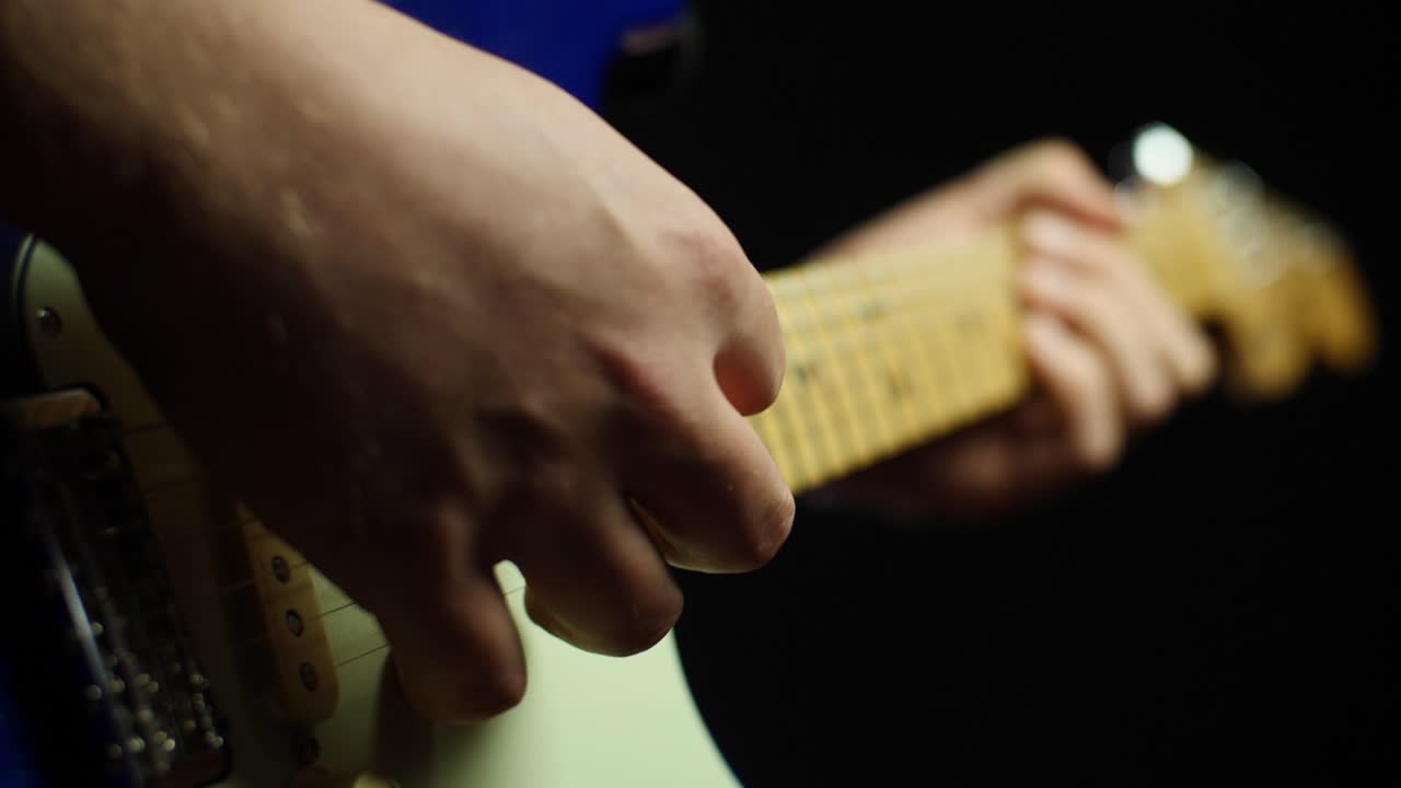 Slow motion close up of an electric guitars neck and strings and guitarists hands while playing notes with a pick. Smooth slow motion with gimbal backward movement. Shot in 4K at 120fps
