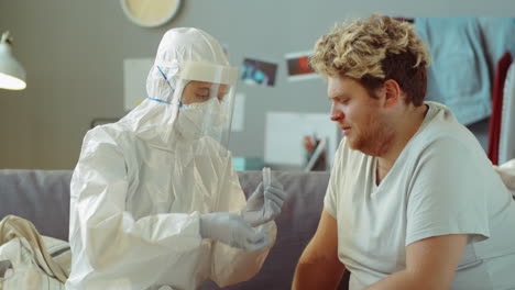 doctor in protective suit taking nasal swab from man at home