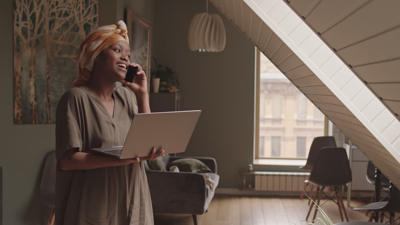Young Black Woman with Laptop Making Phone Call at Home
