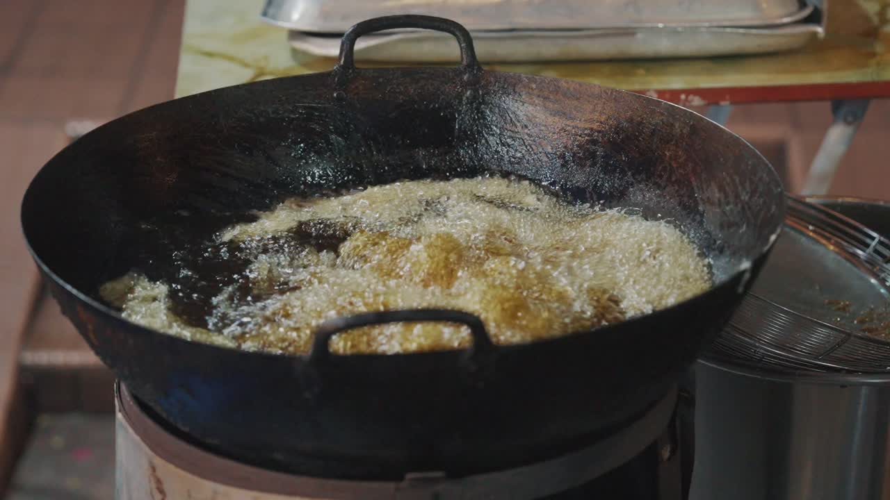 A close-up of a street food hawker's hand placing blocks of white tofu into a large iron wok filled with bubbling, hot cooking oil at a night market