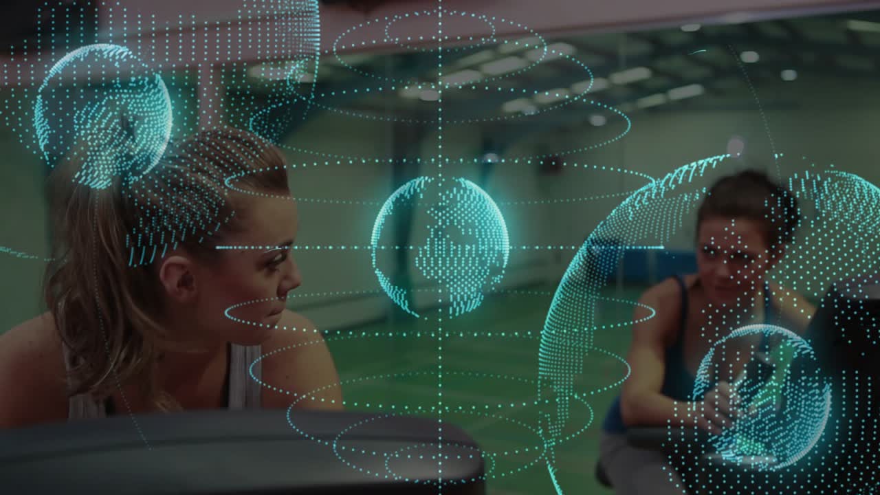 Right woman tapping device, left woman turning smiling in gym with AR globe drifting across faces