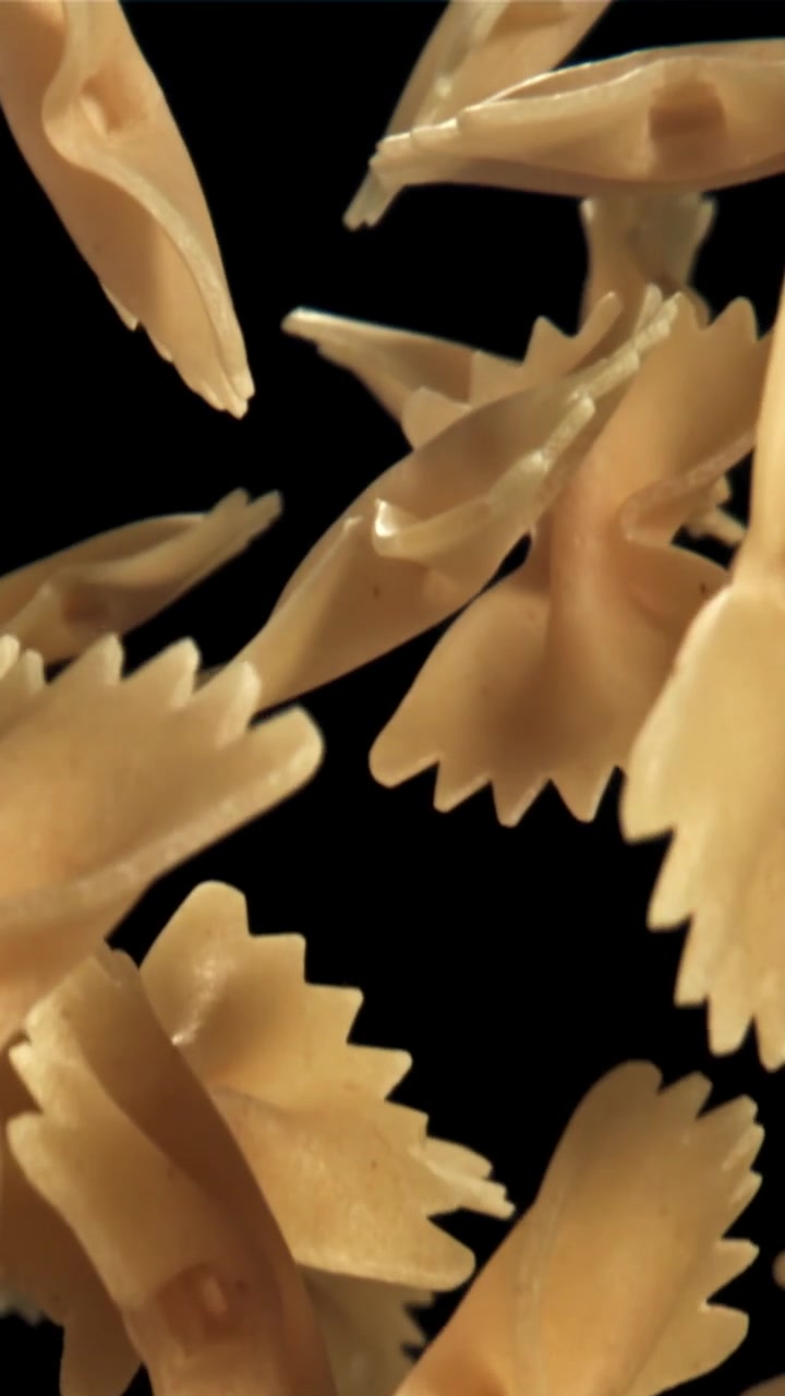Primo piano di pasta farfalle secca che galleggia su sfondo nero