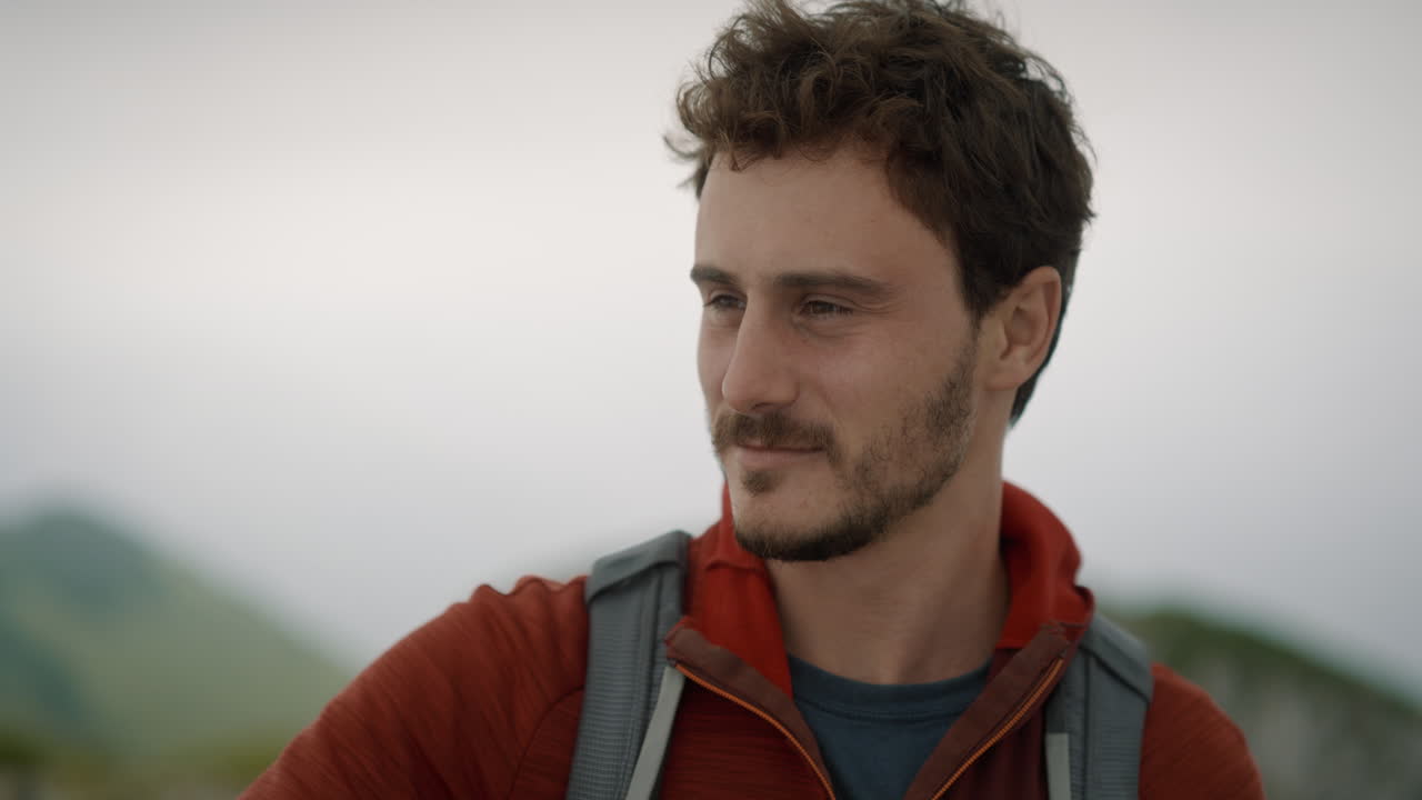 Close up of a young hiker with a backpack and a red jacket, smiling and looking into the distance