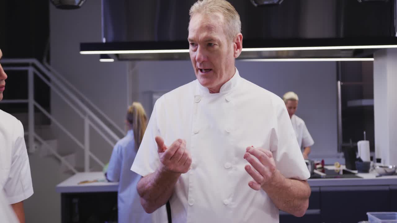 cocinero caucásico profesional en una cocina de un restaurante que enseña a un grupo de chefs aprendices