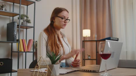 mujer freelancer bebiendo vino después de una conversación remota en línea en una computadora portátil en la oficina de casa