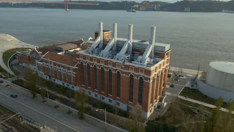 Edificio-De-Fábrica-Industrial-Cerca-Del-Río-Tajo-En-Lisboa,-Portugal,-Filmado-Con-Un-Dron-Durante-La-Puesta-De-Sol