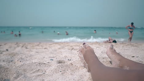 people walk along narrow sand beach against girl legs