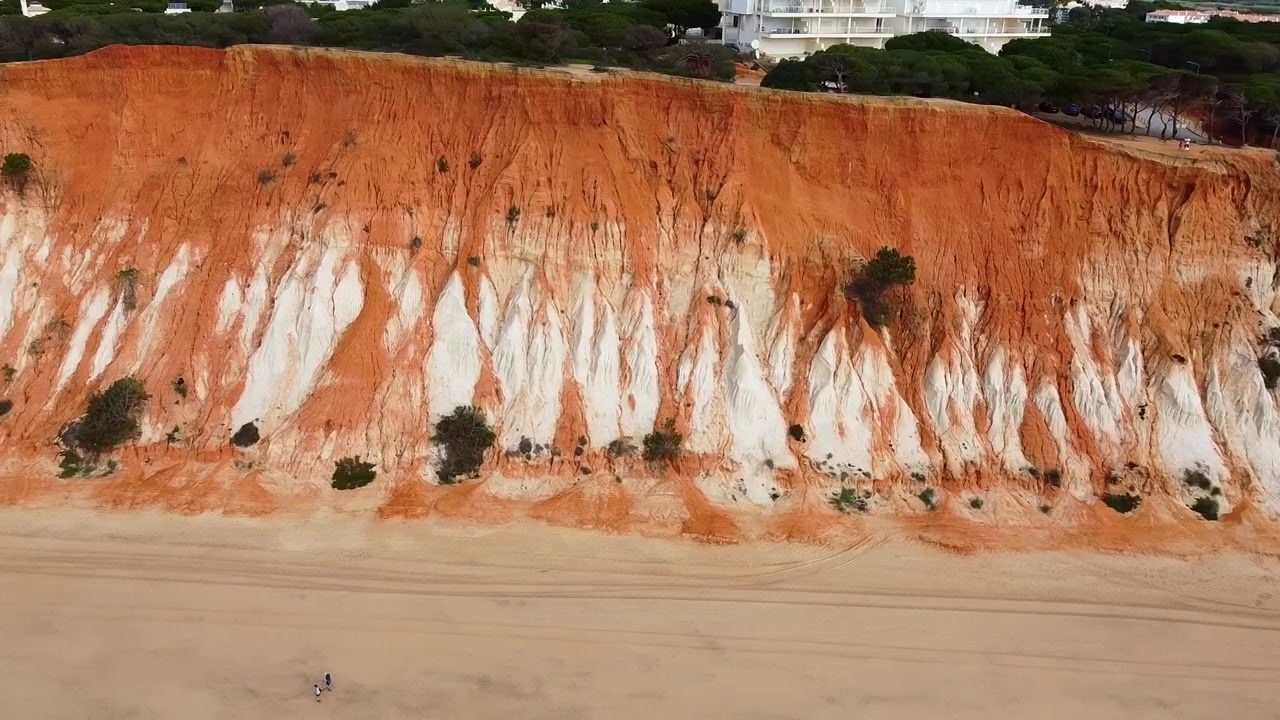 Praia da Falésia. Portugal. Praia com grandes falésias avermelhadas e brancas. Vista aérea em close-up. Falésias e ravinas avermelhadas e brancas da Praia da Falésia. Falésias ao longo de uma longa praia e ondas.