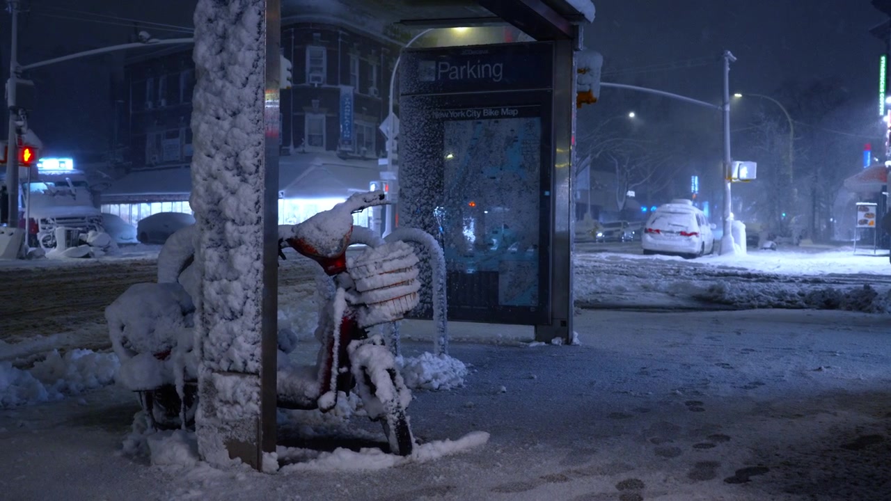 Nova Iorque, EUA, 20 de fevereiro de 2026: Scooter motorizada estacionada perto de mapa de bicicletas da cidade na neve. Pegadas em uma calçada nevada ao lado de uma mobilete coberta e quiosque de informações durante uma nevasca noturna em Nova Iorque.