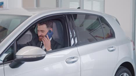 hombre sentado en un coche nuevo y hablando en el móvil en el salón