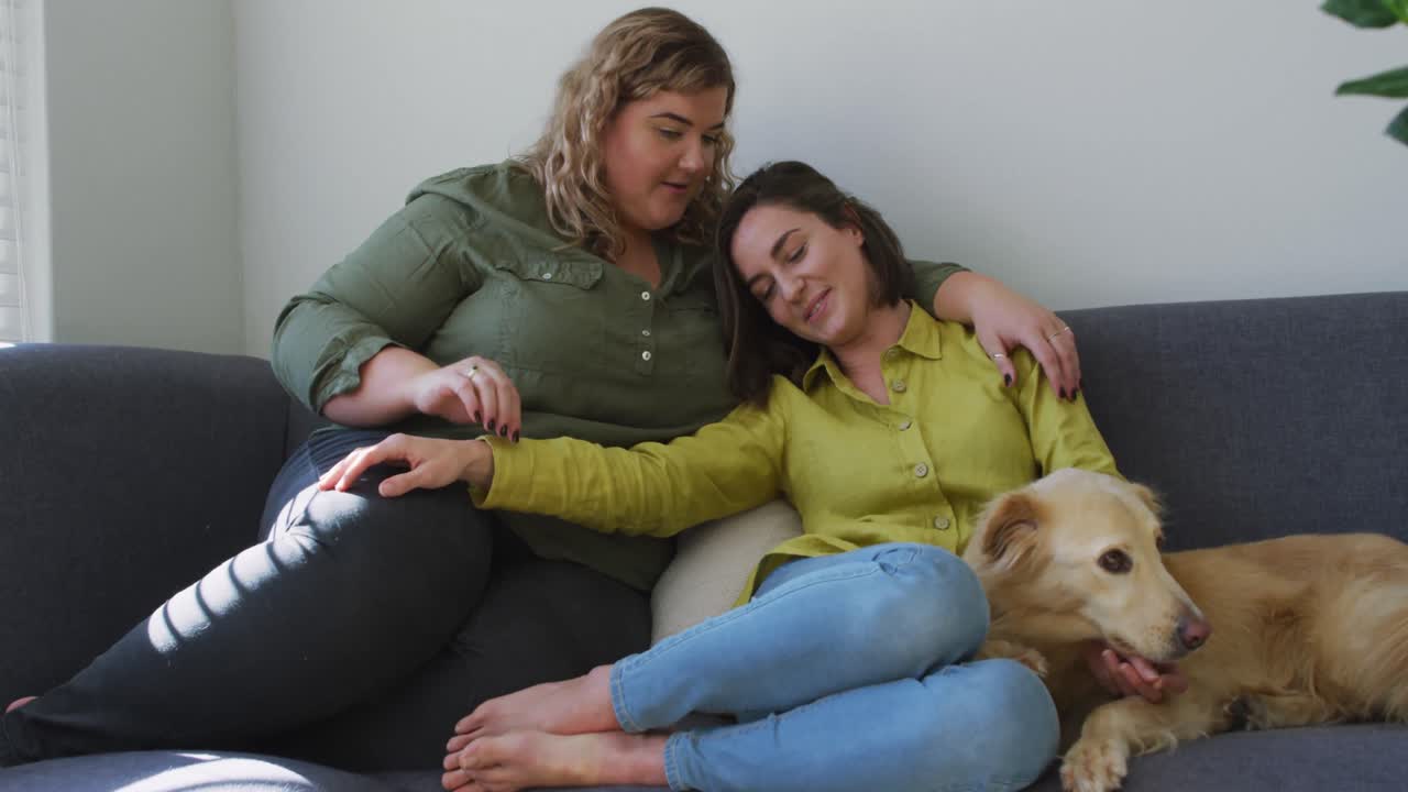 pareja de lesbianas caucásicas sonriendo y sentadas en el sofá con el perro
