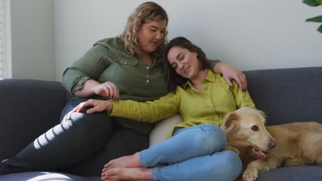 caucasian lesbian couple smiling and sitting on couch with dog