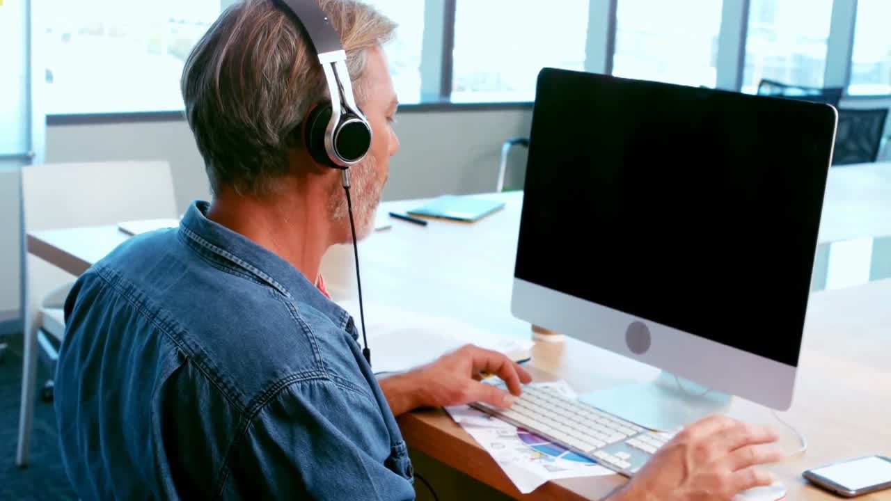 hombre escuchando auriculares mientras trabaja en una computadora de escritorio