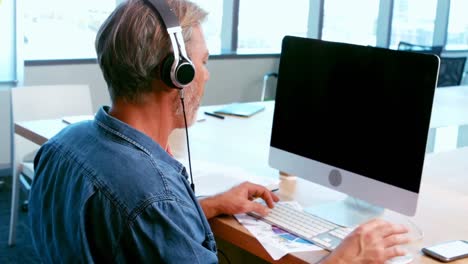 Man-listening-to-headphones-while-working-on-desktop-pc