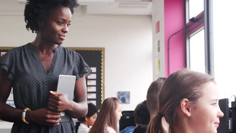 female teacher supervising line of high school students working at screens in computer class