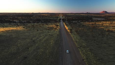 suv blanco conduciendo en un camino de tierra a través de tierras baldías de namibia, puesta de sol en áfrica - vista aérea