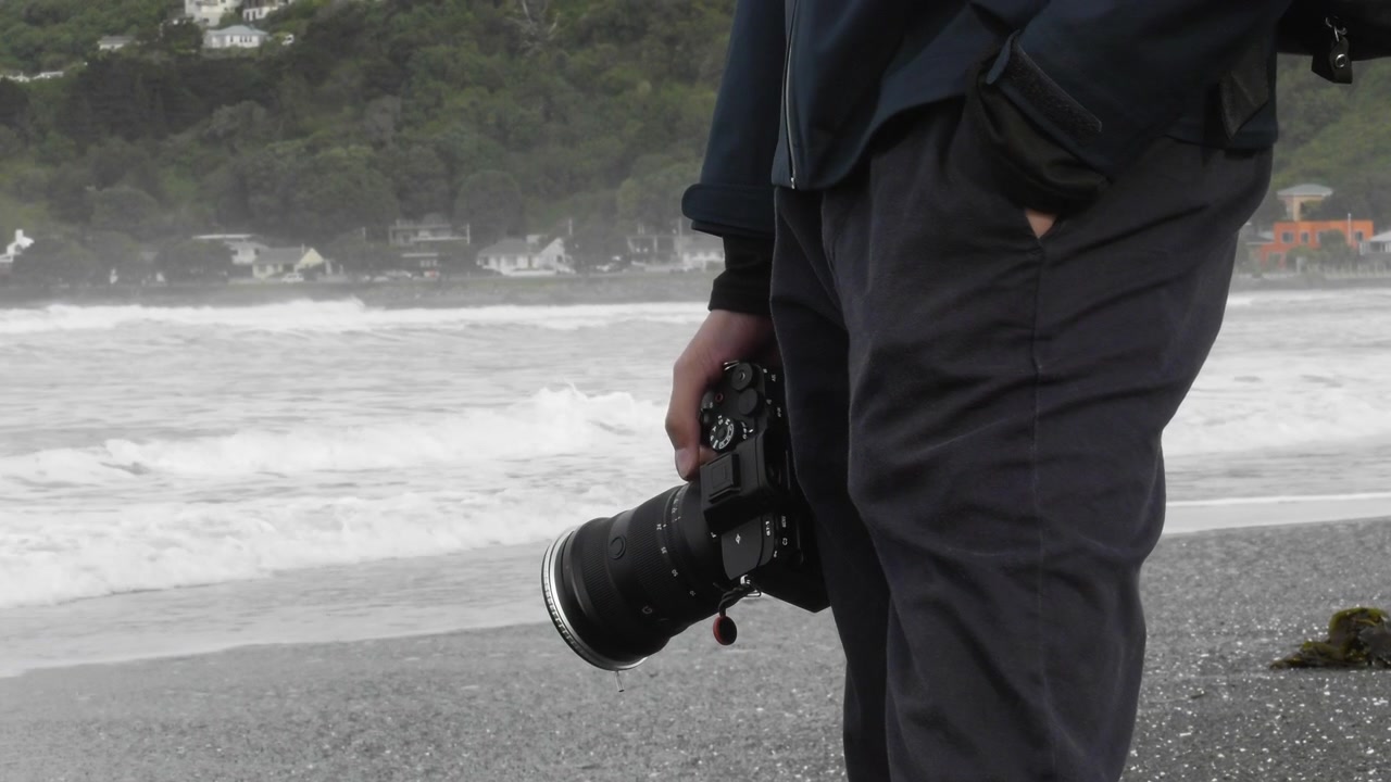 Mano di fotografo uomo che tiene una macchina fotografica sulla costa di Lyall Bay a Wellington, Nuova Zelanda. Primo piano