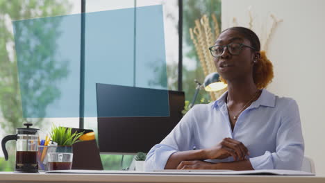 Woman-Looking-At-Projected-Screen-At-Office-Desk-Hosting-Virtual-Online-Meeting