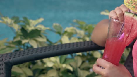 girl mixes frozen drink with curvy stick near green leaves