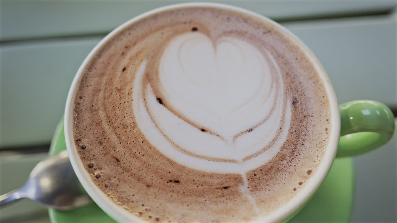 Close up of a cappuccino in a green cup on a table at a terrace