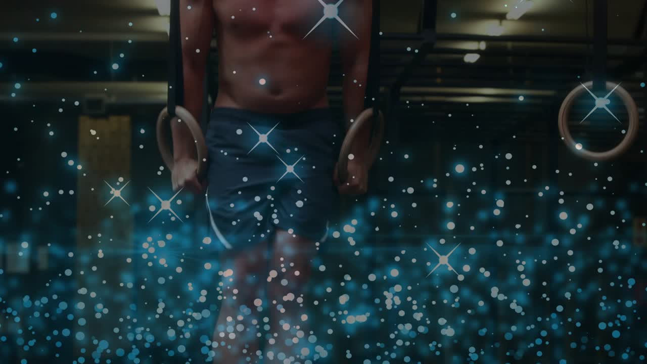 Man gripping rings, starting strength hold in fitness gym while particle sparks obscuring mid torso