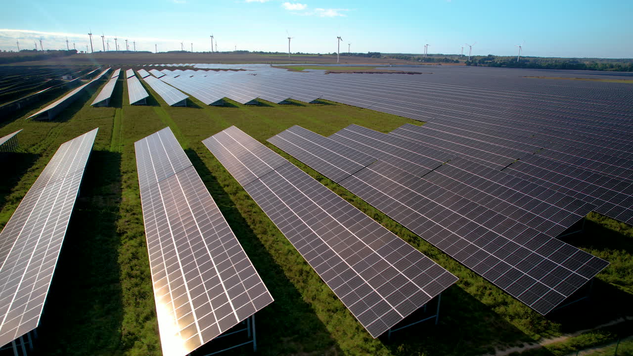 Luftoptagelse af solcellepark med miljøvenlig vindmøllepark i baggrunden om sommeren – Futuristisk koncept for vindenergi og sollys