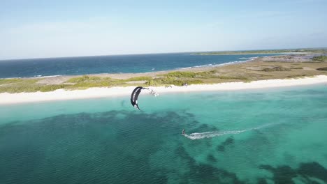 TWO-MEN-jUMP-kitesurf-beachfront-tropical-paradise-ISLAND,-drone-shot-LOS-ROQUES