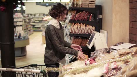 A-girl-weighs-pomelo-on-and-electric-scales-in-a-supermarket-and-puts-a-sticker-with-a-price.-Pomelo-in-a-grid-package.-Side