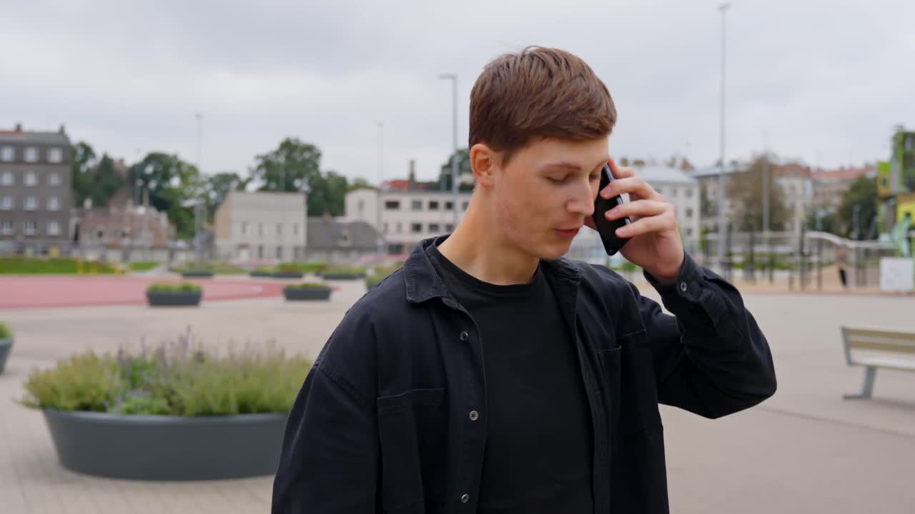 Young man talks on phone while laughing and scratching his head casually walking outdoors