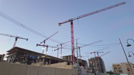 a construction site in paceville, malta, featuring multiple cranes and partially built structures under a clear sky
