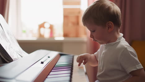 boy in polo shirt plays electrical piano in sunny room