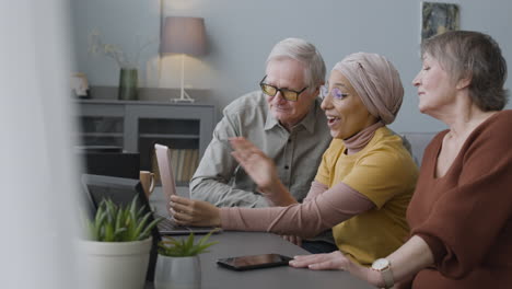 senior couple and a middle aged arabic woman having a video call via tablet while sitting together in the living room at home