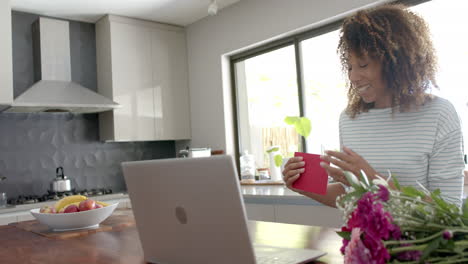 feliz mujer biracial teniendo video llamada del día de san valentín en la computadora portátil en casa soplando beso, cámara lenta