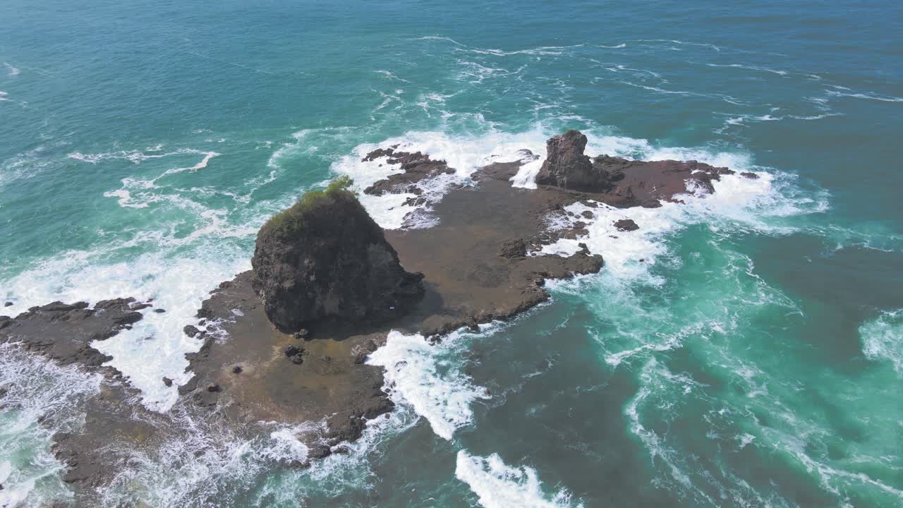 Aerial top down shot showing waves of ocean crashing and flooding Watu Lumbung Beach in Indonesia