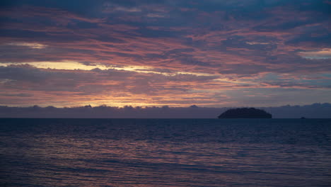 pink and purple color beach sunset over sea with sunlight reflected in water and cloudy sky, silhouetted sulug islet in background, malaysia, kota kinabalu